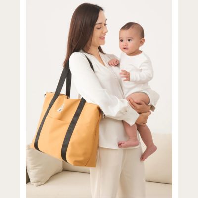 Femme-porte-sac-a-langer-décontracté-sur-une-épaule-et-bébé-dans-ses-bras